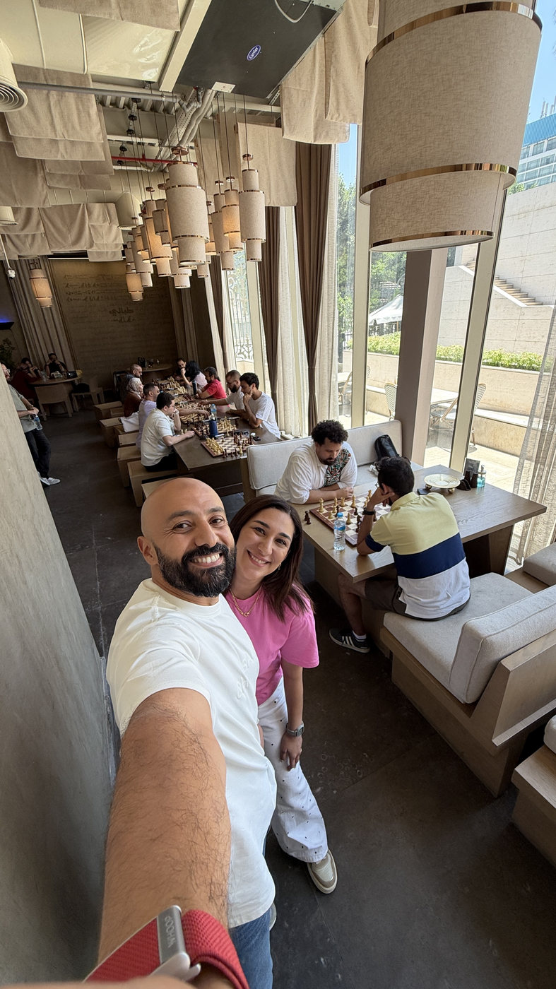Nora and Sherif at a gathering, with players at the tables behind them